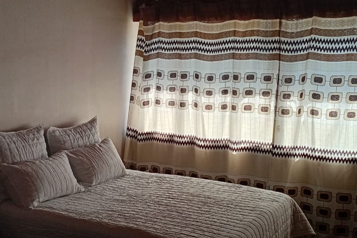 A bedroom featuring a window with patterned curtains, providing natural light and a simple, functional layout.