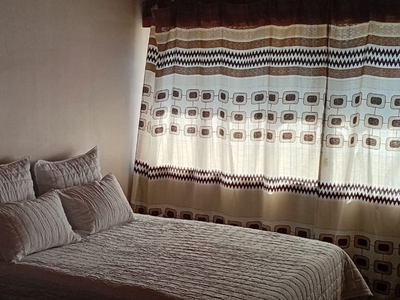 A bedroom featuring a window with patterned curtains, providing natural light and a simple, functional layout.