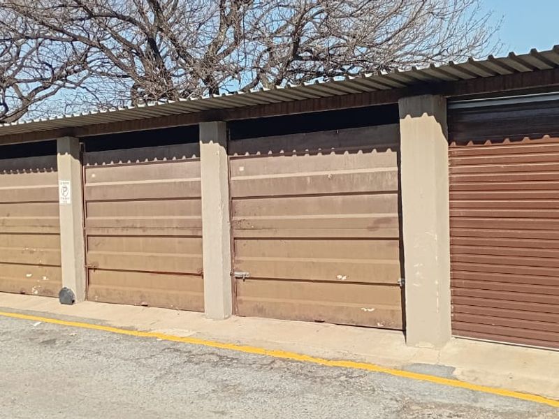 A row of functional metal garage units featuring corrugated roofing and concrete structural pillars, showing signs of exterior wear.