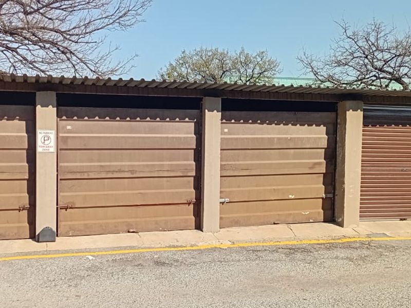 A row of functional metal garage units with corrugated roofing, providing secure off-street parking for the property.