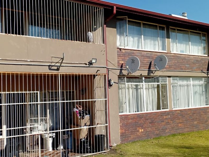 Rear elevation of a multi-story flat complex featuring brick and plaster finishes, security bars on balconies, and multiple satellite dish installations.