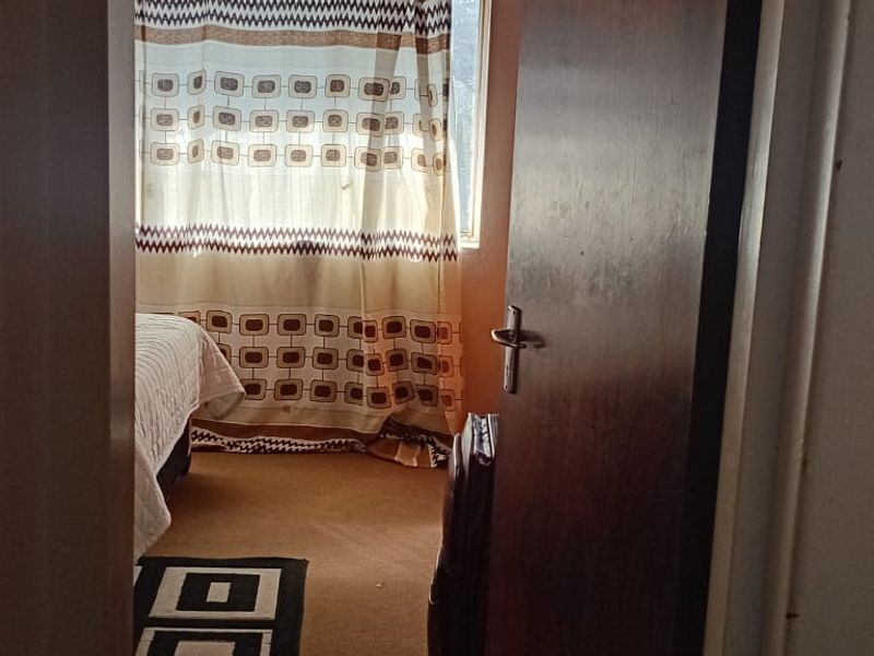 A view into a bedroom featuring a window with curtains and a wooden door frame.