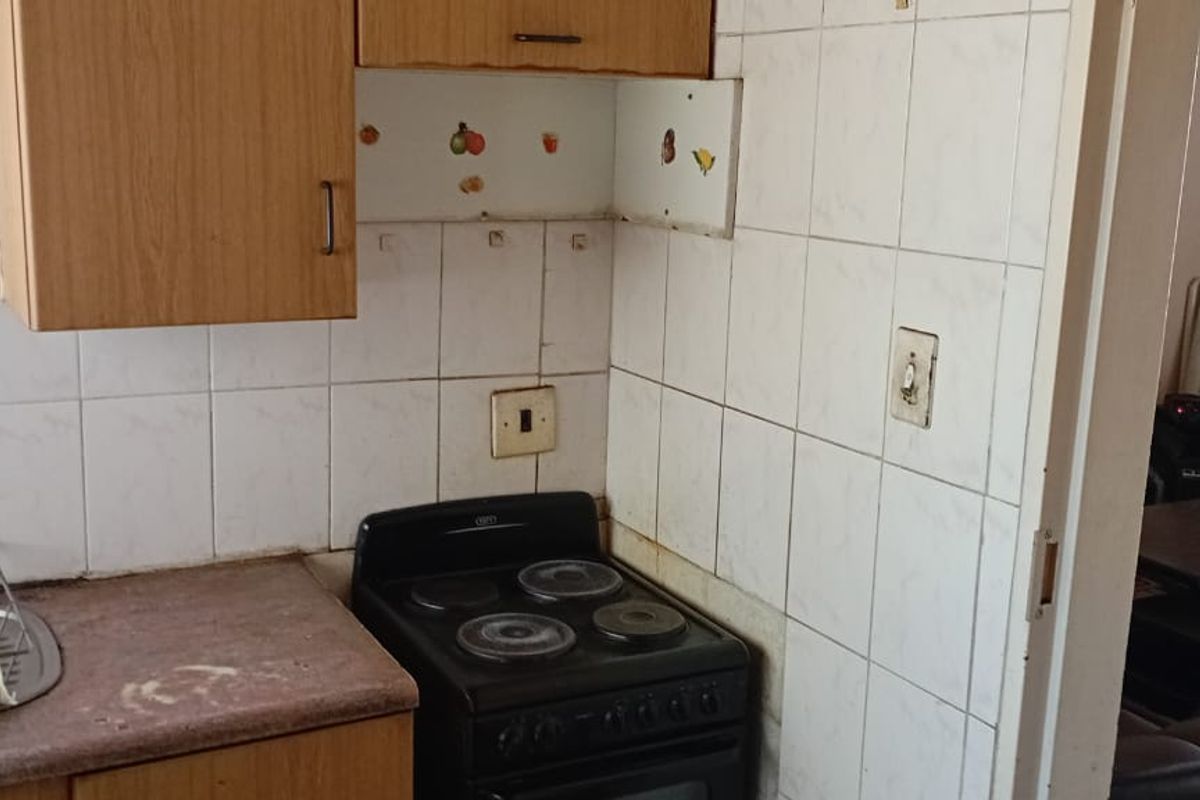 A compact kitchen area featuring built-in cabinetry, a tiled splashback, and a freestanding stove, requiring cosmetic updates to improve its overall condition.
