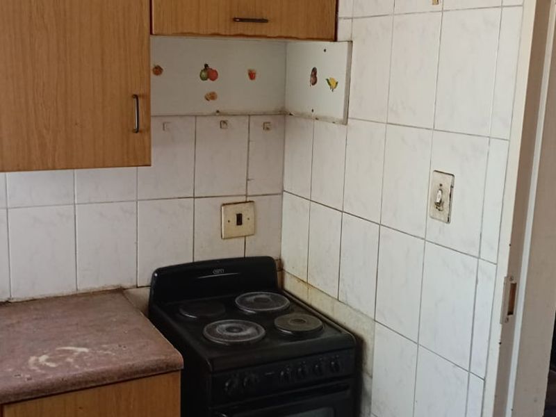 A compact kitchen area featuring built-in cabinetry, a tiled splashback, and a freestanding stove, requiring cosmetic updates to improve its overall condition.