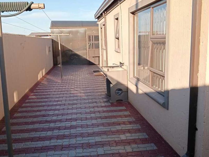 A paved rear exterior area featuring a utility sink, security bars on windows, and a perimeter boundary wall.