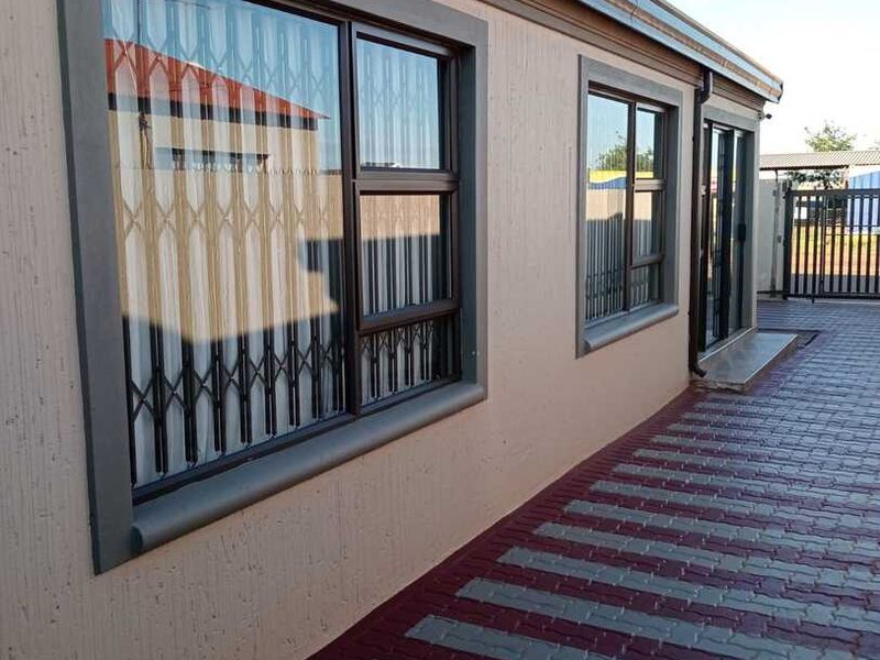 A well-maintained rear exterior view featuring paved ground, aluminium window frames with security gates, and a sliding door entrance.