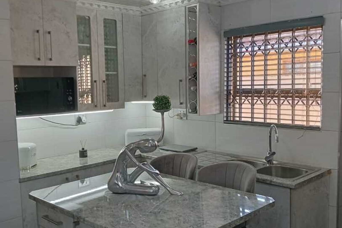 Modern kitchen featuring stone countertops, built-in cabinetry, a central island, and integrated microwave, finished with contemporary track lighting and tiled surfaces.