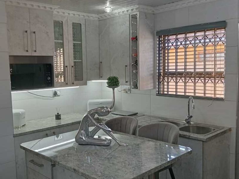 Modern kitchen featuring stone countertops, built-in cabinetry, a central island, and integrated microwave, finished with contemporary track lighting and tiled surfaces.