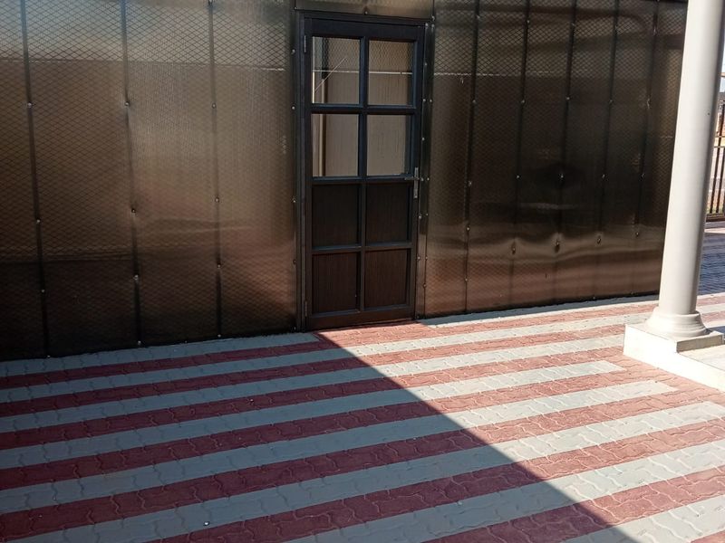 A covered patio area featuring a durable polycarbonate enclosure and patterned paved flooring, providing a functional outdoor space.