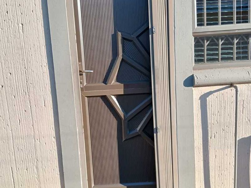 Front entrance featuring a decorative brown security gate and a window with integrated security bars on a textured exterior wall.