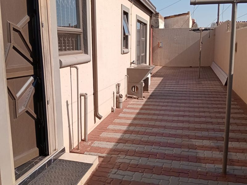 A paved rear exterior area featuring a utility sink, security gate, and window security bars along the side of the house.
