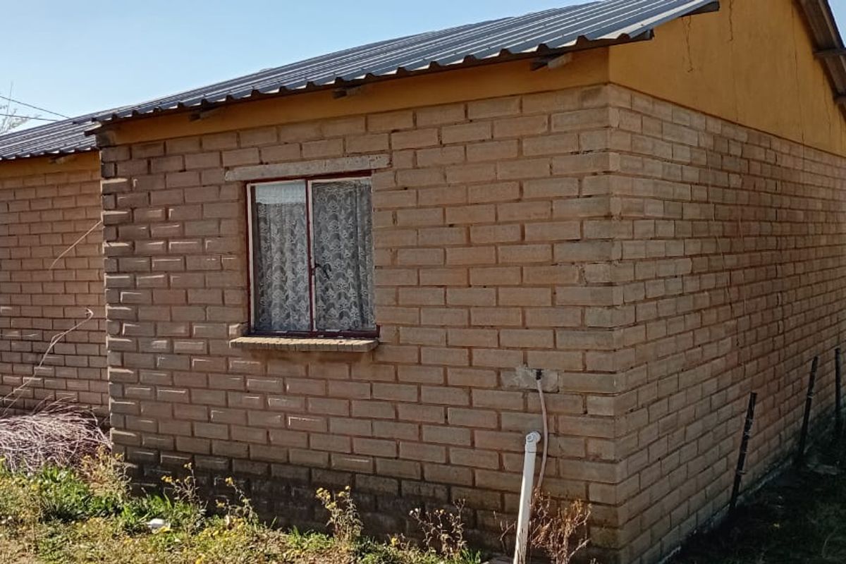 A view of the rear exterior of a modest brick house featuring a corrugated metal roof and steel window frames.