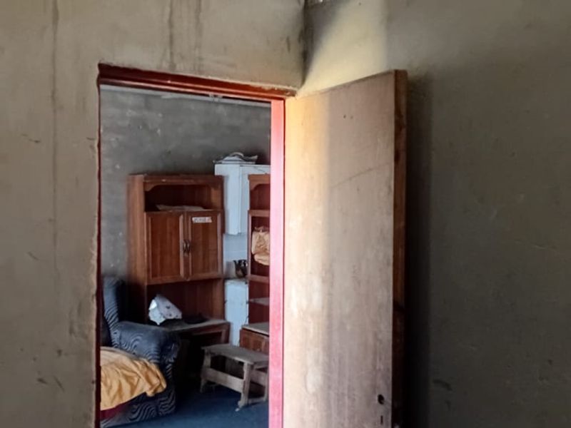 A view through a doorway into an adjacent room, featuring unfinished plaster walls and basic interior door construction.