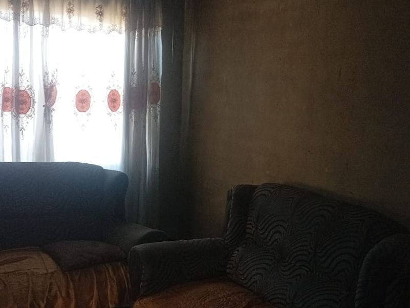 A dimly lit living room space featuring plain wall finishes and window treatments, requiring cosmetic updates to improve the overall aesthetic and brightness.