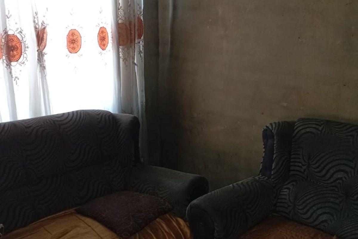 A living room area featuring unfinished wall surfaces and natural light through window curtains.