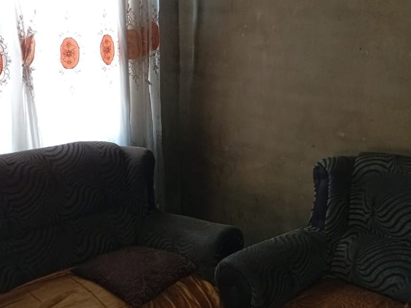 A living room area featuring unfinished wall surfaces and natural light through window curtains.