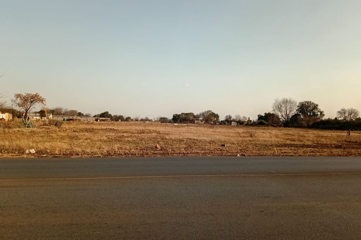 A view of an undeveloped small holding plot adjacent to a paved road, showcasing the open landscape and surrounding area.