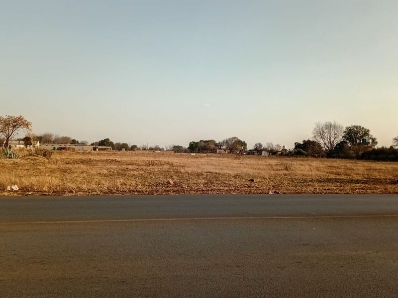 A view of an undeveloped small holding plot adjacent to a paved road, showcasing the open landscape and surrounding area.