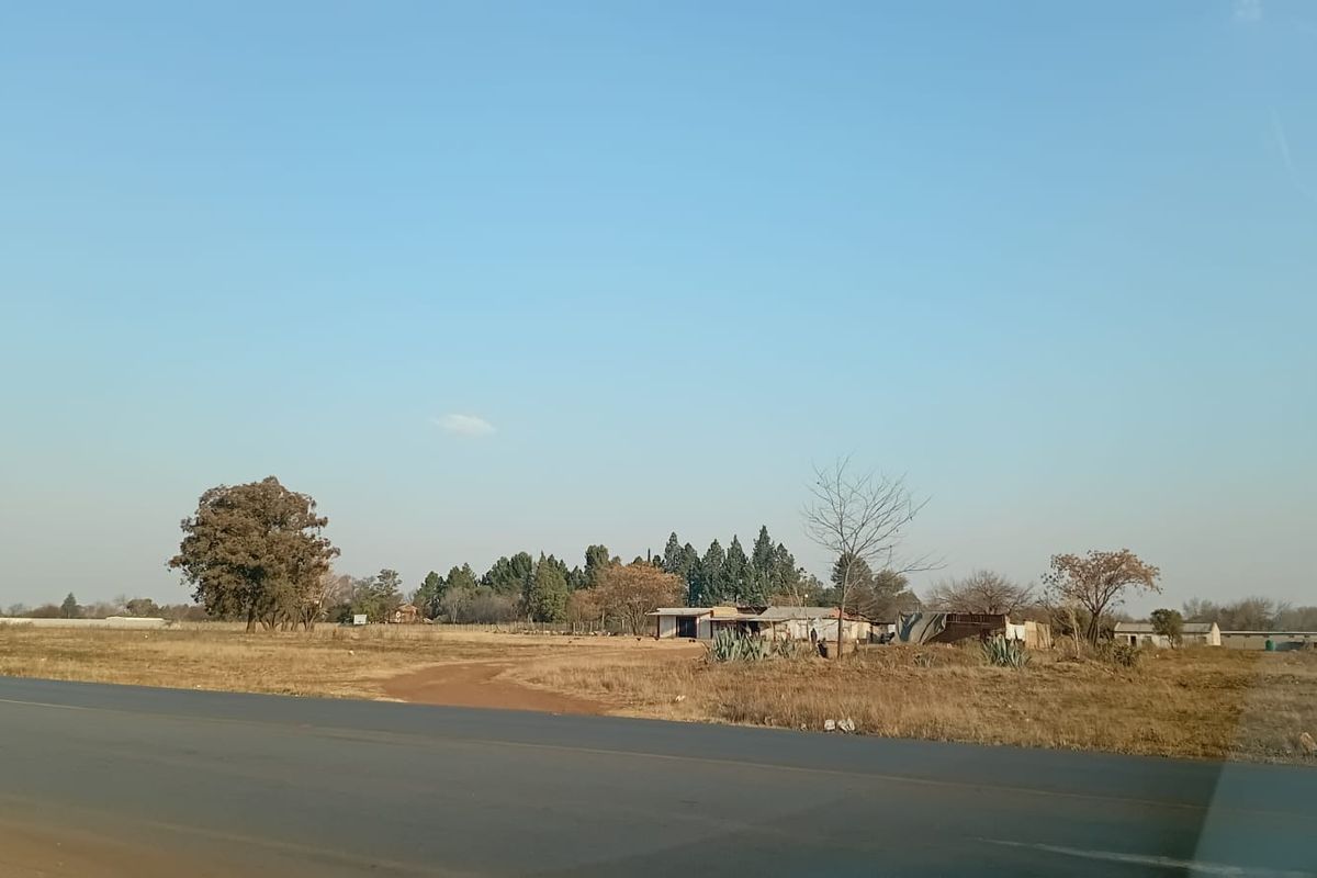 A view of the small holding property from the adjacent asphalt road, showing the open land and existing outbuildings.