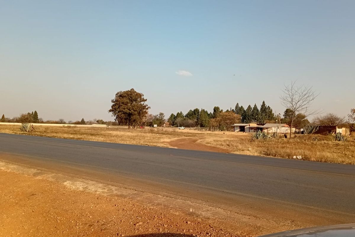 A view of the small holding property from the adjacent asphalt road, showing the surrounding landscape and existing outbuildings.