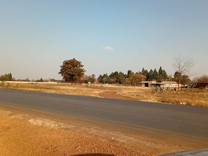 A view of the small holding property from the adjacent asphalt road, showing the surrounding landscape and existing outbuildings.