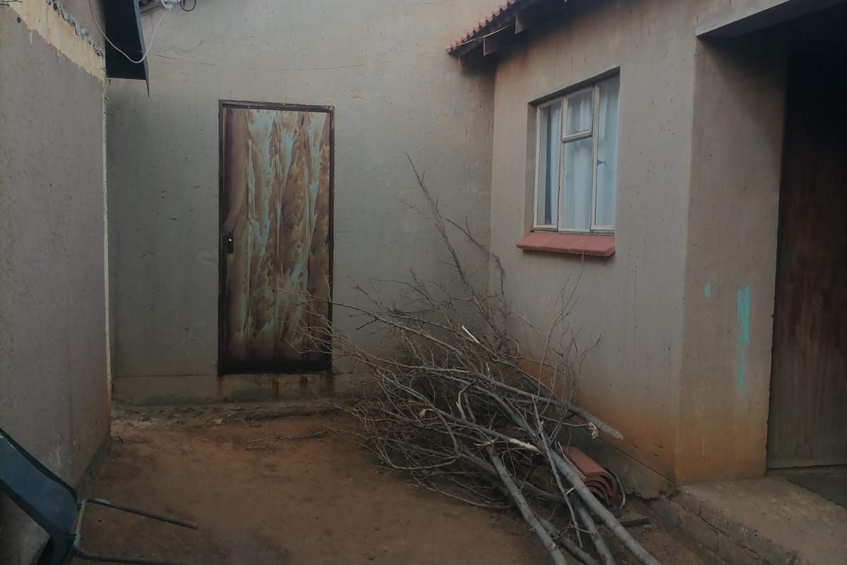 Rear exterior view of the property showing a small courtyard area with a metal door, tiled roof sections, and a satellite dish.