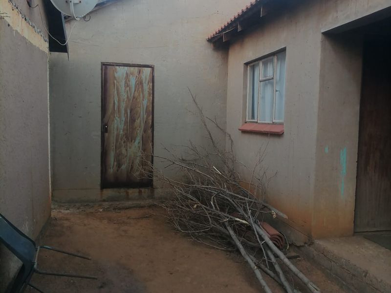 Rear exterior view of the property showing a small courtyard area with a metal door, tiled roof sections, and a satellite dish.