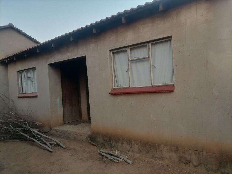 Rear exterior view of a single-story house featuring a tiled roof and metal window frames, showing signs of significant weathering and exterior wear.