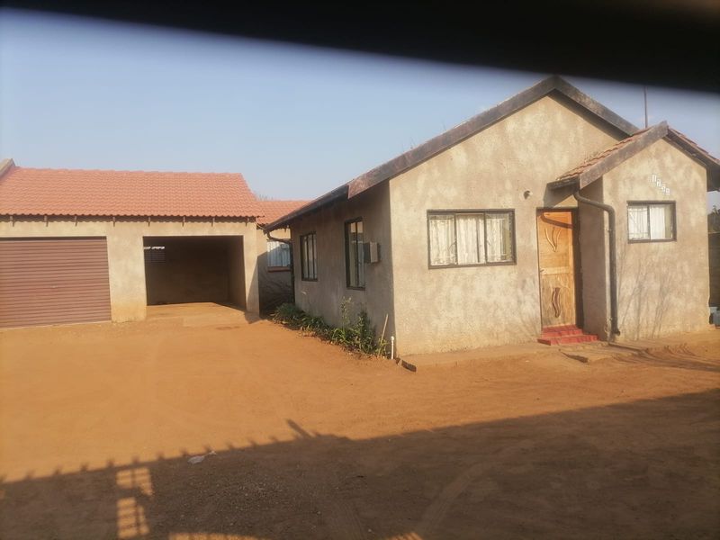 Front view of a single-story house featuring a detached garage, unpaved driveway, and unpainted exterior walls with tiled roofing.