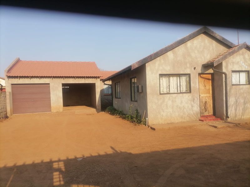 Front view of a single-story house featuring a tiled roof, a garage, a carport, and an unpaved driveway area.