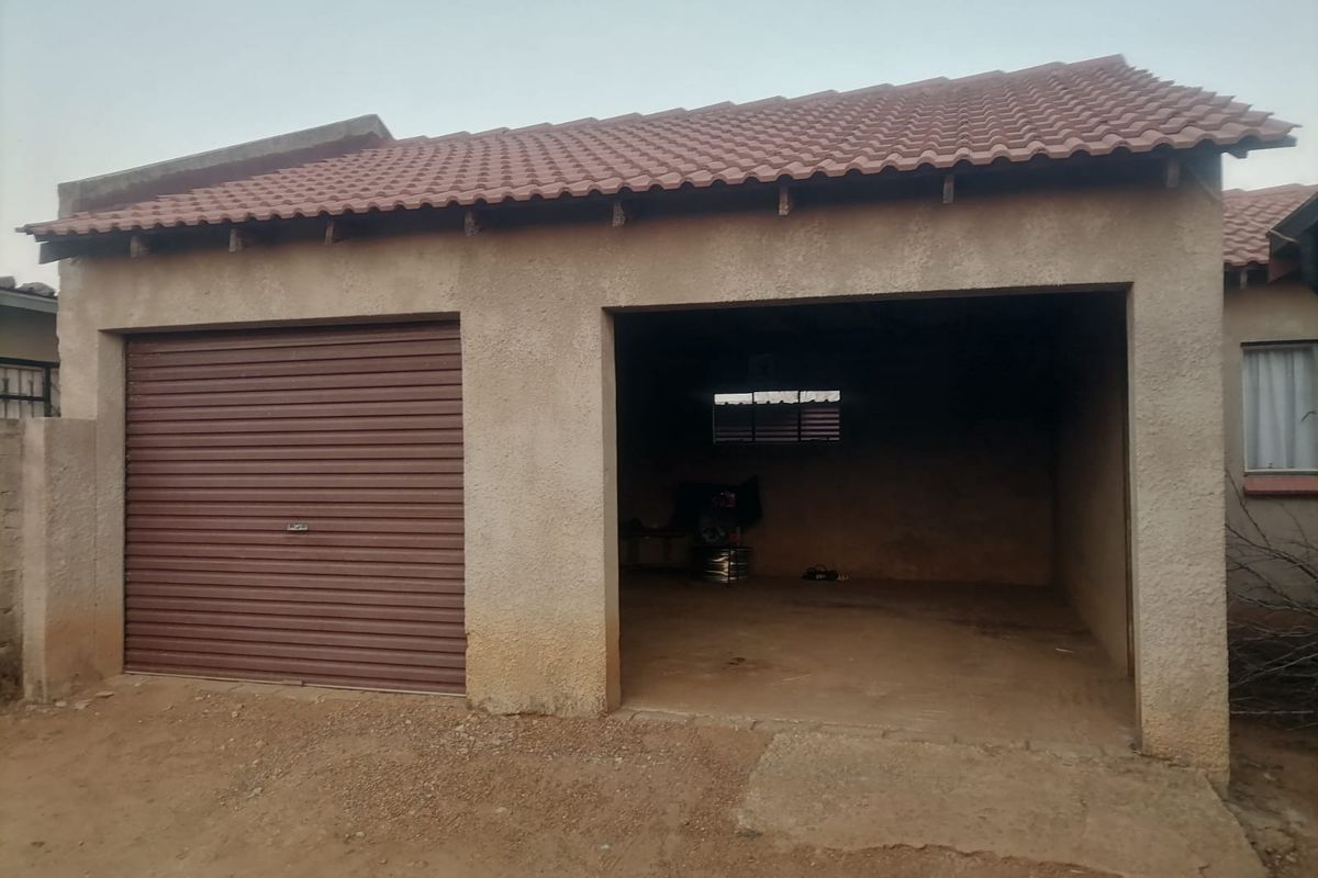 A double garage structure featuring one roller shutter door and one open bay with a tiled roof and concrete flooring.