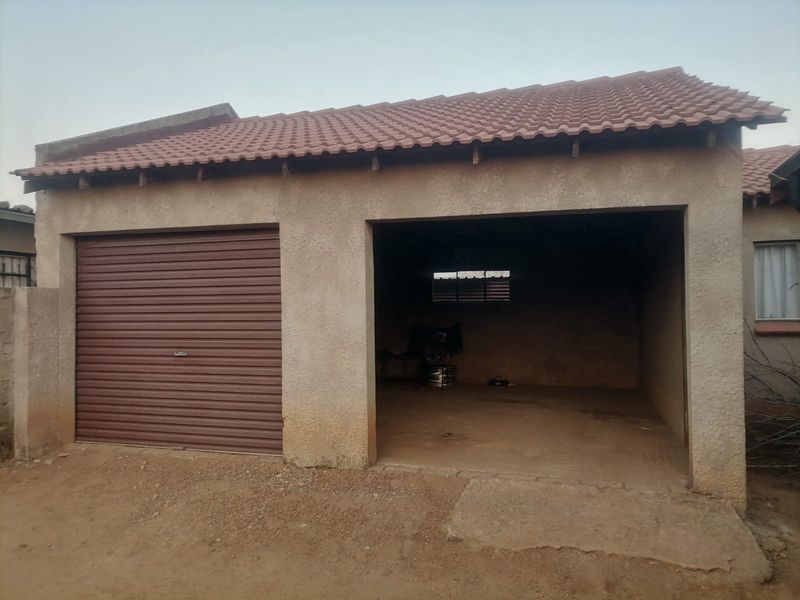 A double garage structure featuring one roller shutter door and one open bay with a tiled roof and concrete flooring.