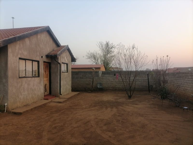 Rear view of a detached house featuring a concrete block boundary wall, unpainted plaster finish, and a spacious, undeveloped backyard area.