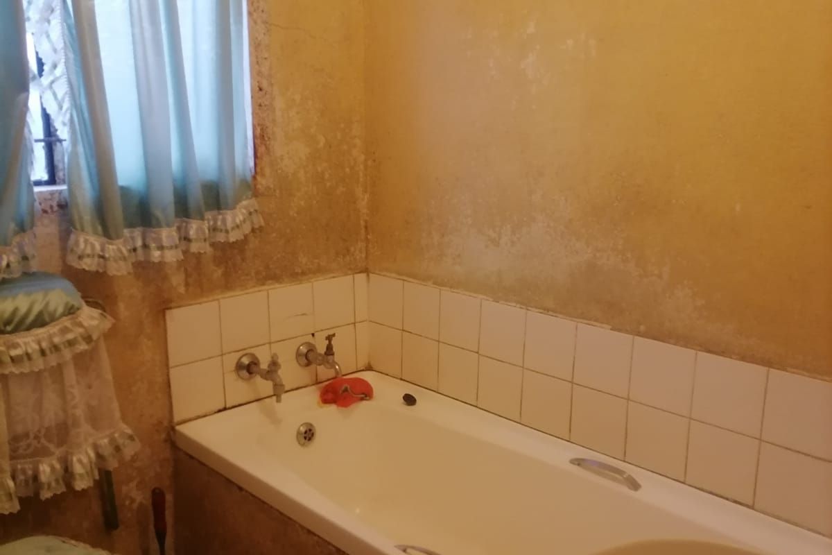 A dated bathroom featuring a built-in bathtub with wall-mounted fixtures, requiring significant cosmetic renovation and wall surface repairs.