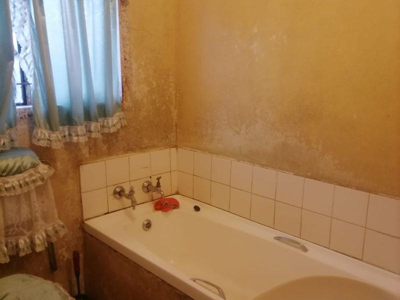 A dated bathroom featuring a built-in bathtub with wall-mounted fixtures, requiring significant cosmetic renovation and wall surface repairs.