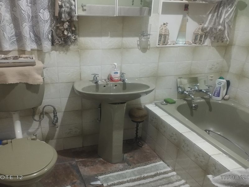 A dated bathroom featuring a pedestal basin, bathtub, and toilet with original wall and floor tiling, offering significant potential for a modern renovation.