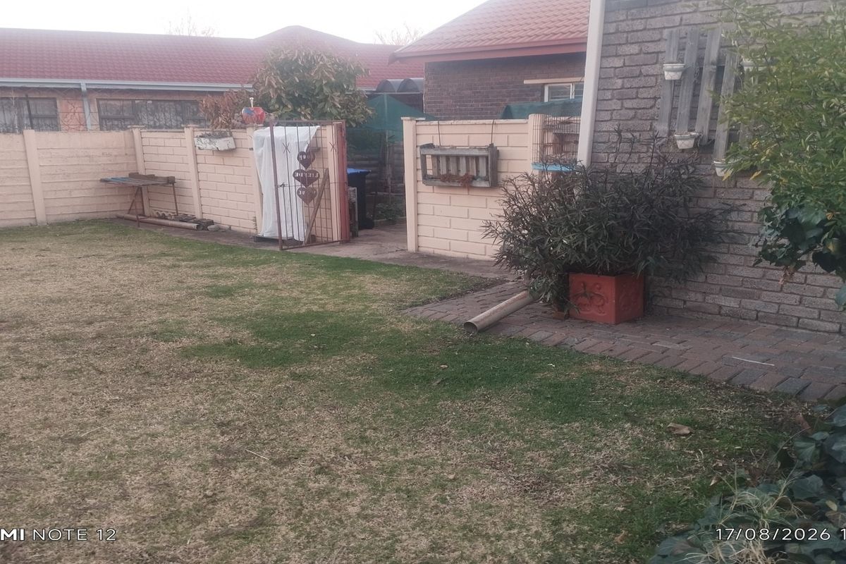 A rear garden area featuring a brick boundary wall, paved walkway, and lawn space adjacent to the main house structure.