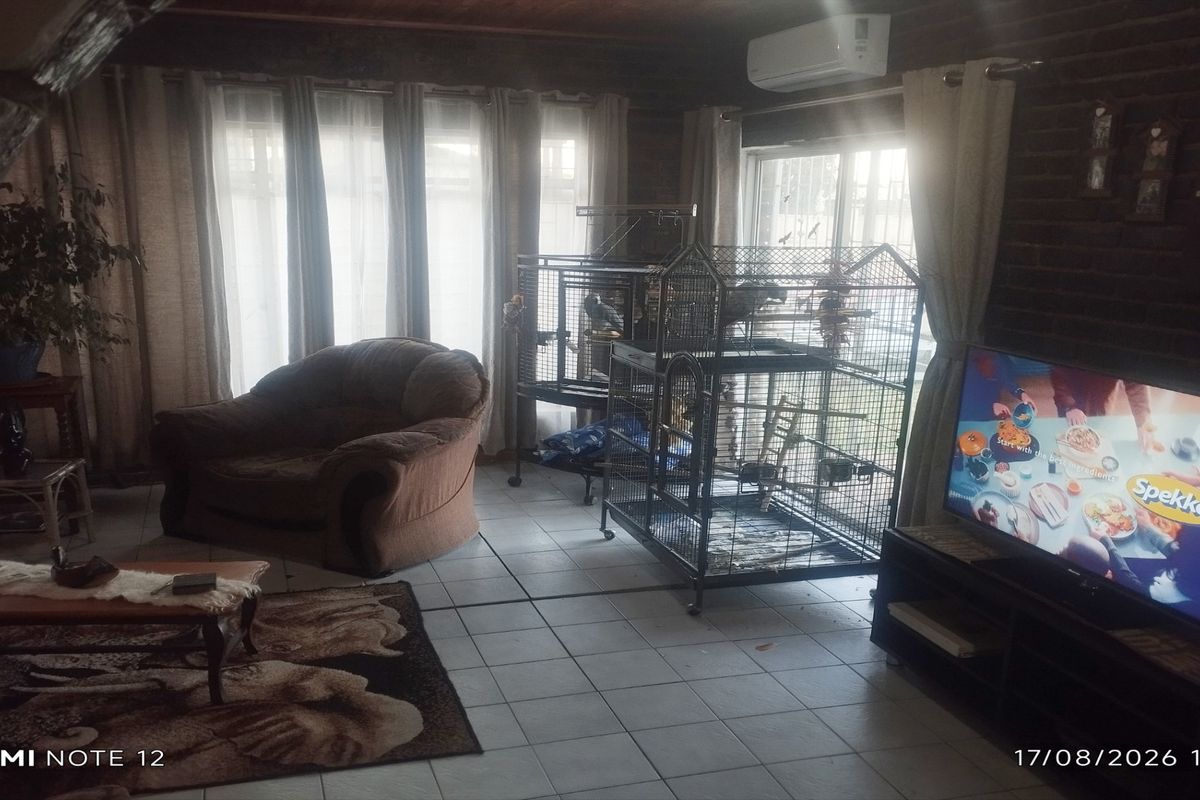 A living room featuring tiled flooring, exposed timber ceilings, and sliding glass doors providing natural light.