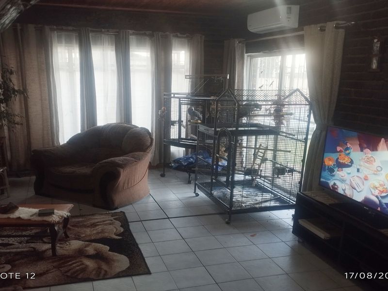 A living room featuring tiled flooring, exposed timber ceilings, and sliding glass doors providing natural light.