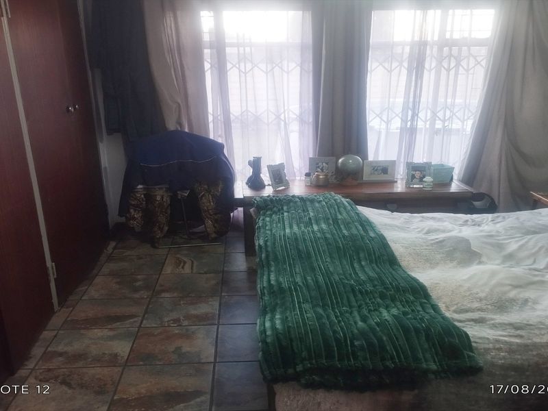 A bedroom featuring tiled flooring and built-in cupboards, with natural light entering through windows fitted with security gates.