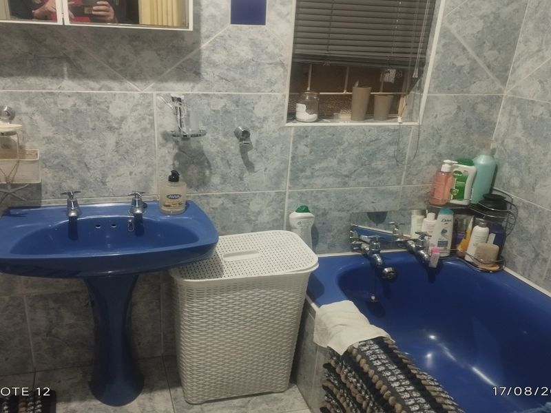 A bathroom featuring blue sanitaryware, including a pedestal basin and bathtub, with full-height wall tiling and a window.