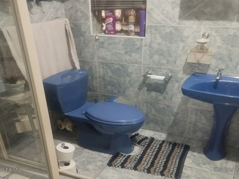 A dated bathroom featuring blue sanitaryware, including a pedestal basin and toilet, with tiled walls and a glass shower enclosure.