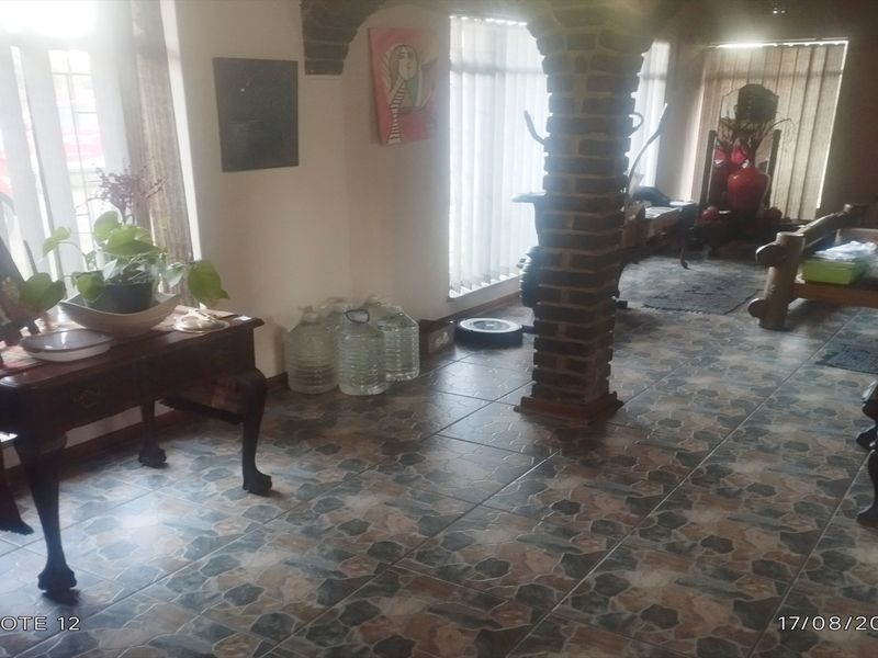 A living area featuring a distinctive brick archway, tiled flooring, and large windows with vertical blinds, offering a dated but functional layout.