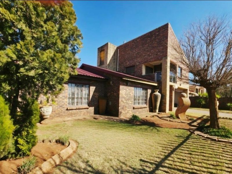 A multi-level face brick house featuring a metal roof, a balcony with glass balustrades, and a well-maintained front garden.