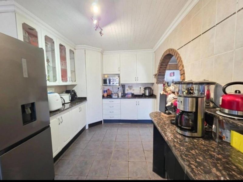 A functional kitchen featuring white cabinetry, granite countertops, tiled flooring, and a distinctive brick archway leading to the adjacent living space.