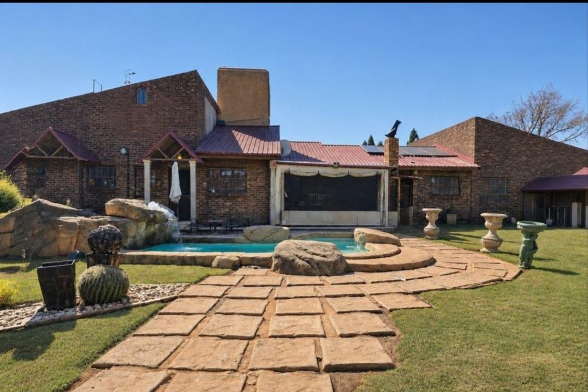Rear exterior view featuring a brick house with a metal roof, a swimming pool with rock features, and a stone-paved pathway in the garden.