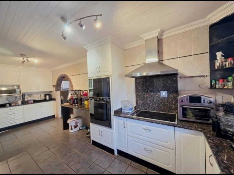 Spacious kitchen featuring granite countertops, built-in oven, electric hob with extractor fan, and ample cabinetry, finished with tiled flooring and a classic ceiling design.