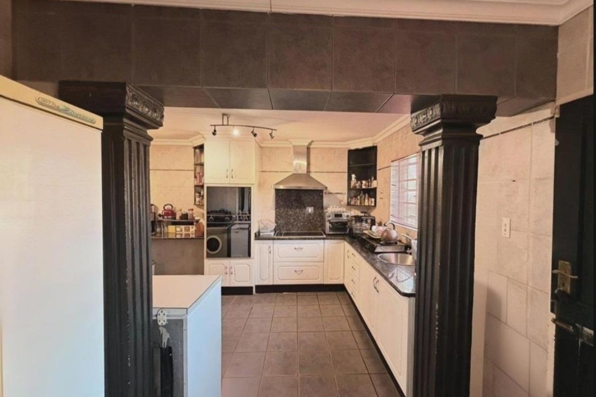 A functional kitchen featuring white cabinetry, granite countertops, built-in oven, stainless steel extractor fan, and tiled flooring, framed by decorative columns.