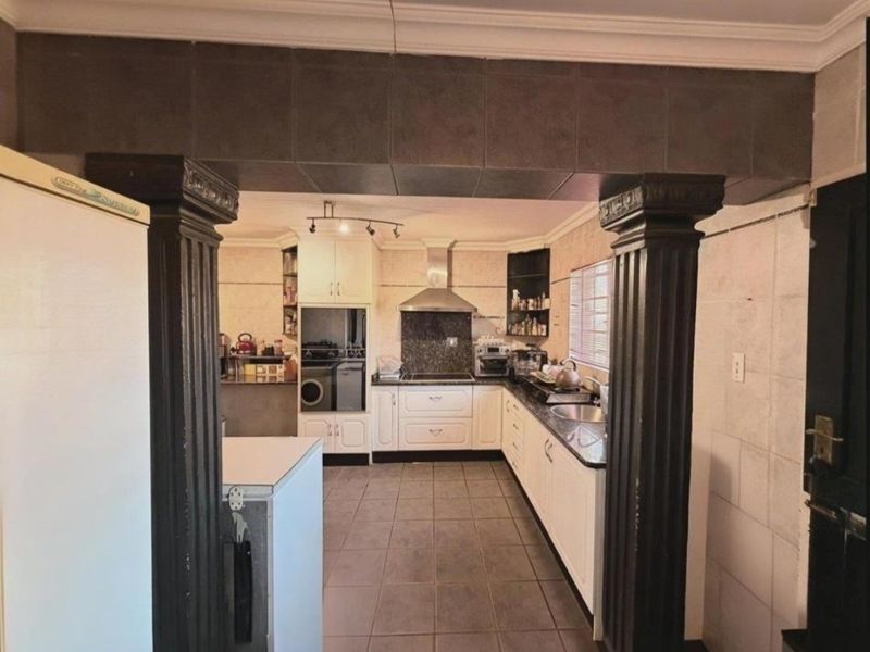 A functional kitchen featuring white cabinetry, granite countertops, built-in oven, stainless steel extractor fan, and tiled flooring, framed by decorative columns.