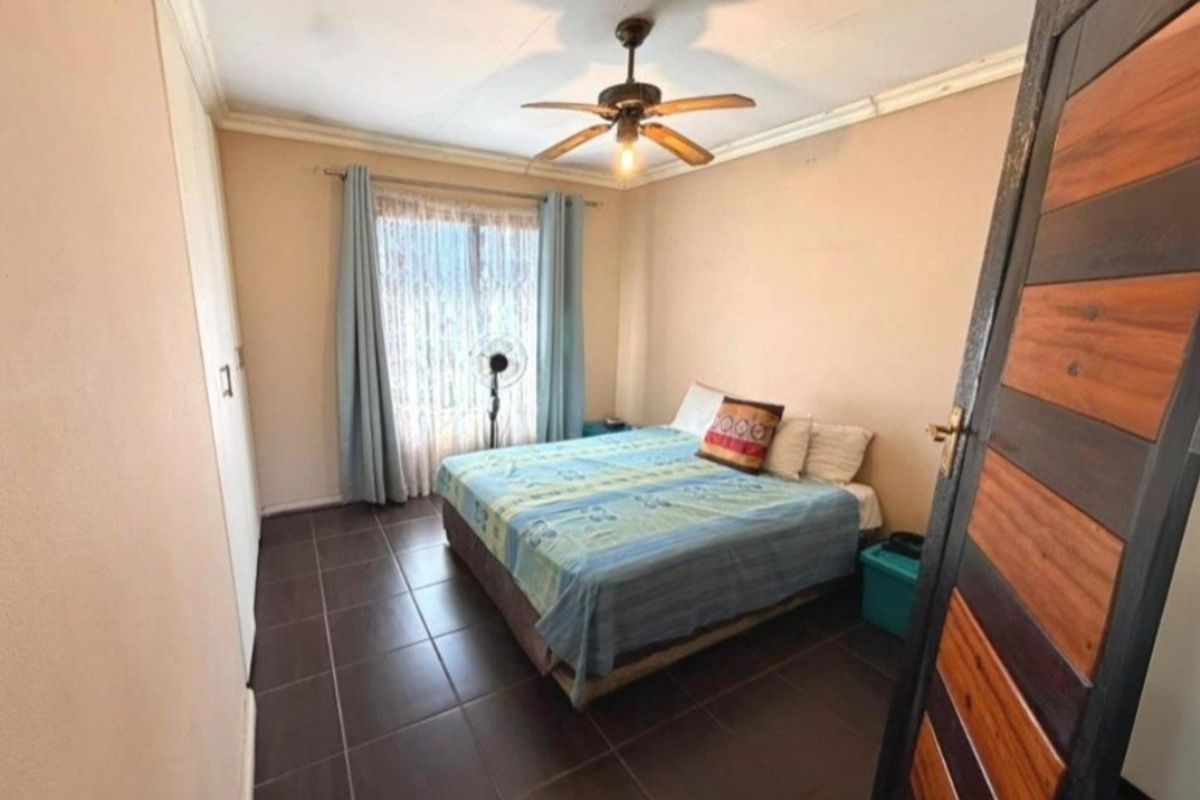 A functional bedroom featuring tiled flooring, a ceiling fan, and a built-in wardrobe, providing a practical and comfortable living space.
